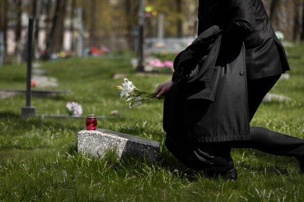 Людина кладе квіти на могилу / Фото: Freepik