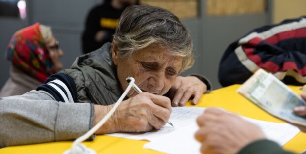 Пенсионерка, подписывающая документ на получение денег