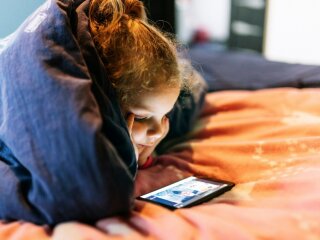 Дівчинка лежить у ліжку з телефоном / фото: Freepik