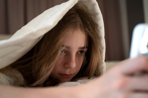 Девушка лежит в кровати с телефоном / фото: Freepik