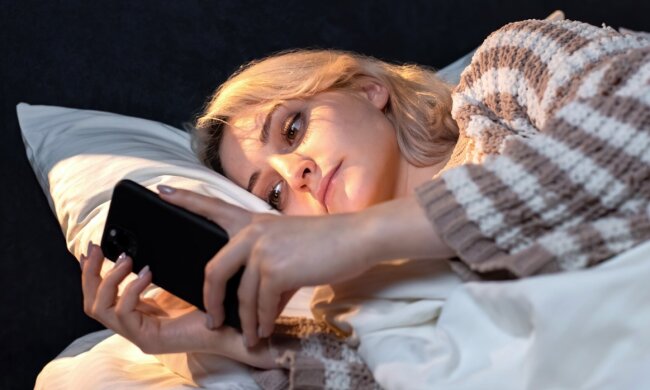 Девушка лежит в кровати с телефоном / фото: Freepik